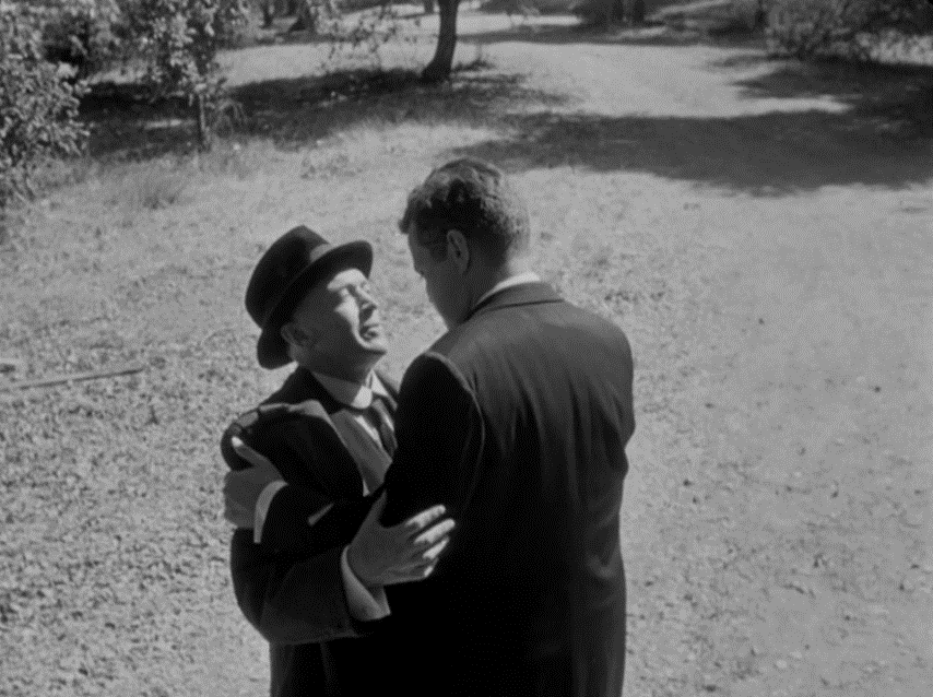 A wide shot of two men facing one another, with open space on either side of them.